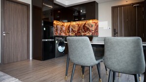 Eine moderne Küche mit dunklen Schränken, einer Marmor-Spritzschutzwand und einem eingebauten Backofen. Vor einem Esstisch befinden sich zwei graue Polsterstühle.