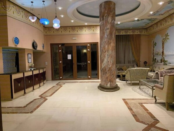 Un hall d’entrée avec une colonne en marbre, un comptoir d’accueil et un espace détente comprenant des canapés et une table basse.