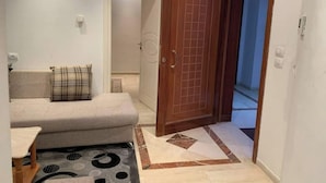 Una stanza piccola e accogliente con un divano, un tappeto decorato e una porta in legno che dà su un'altra stanza.