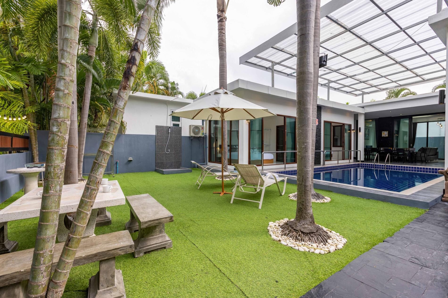 A modern outdoor area with a pool, lounge chairs, and a covered patio.