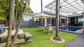A modern outdoor area with a pool, lounge chairs, and a covered patio.