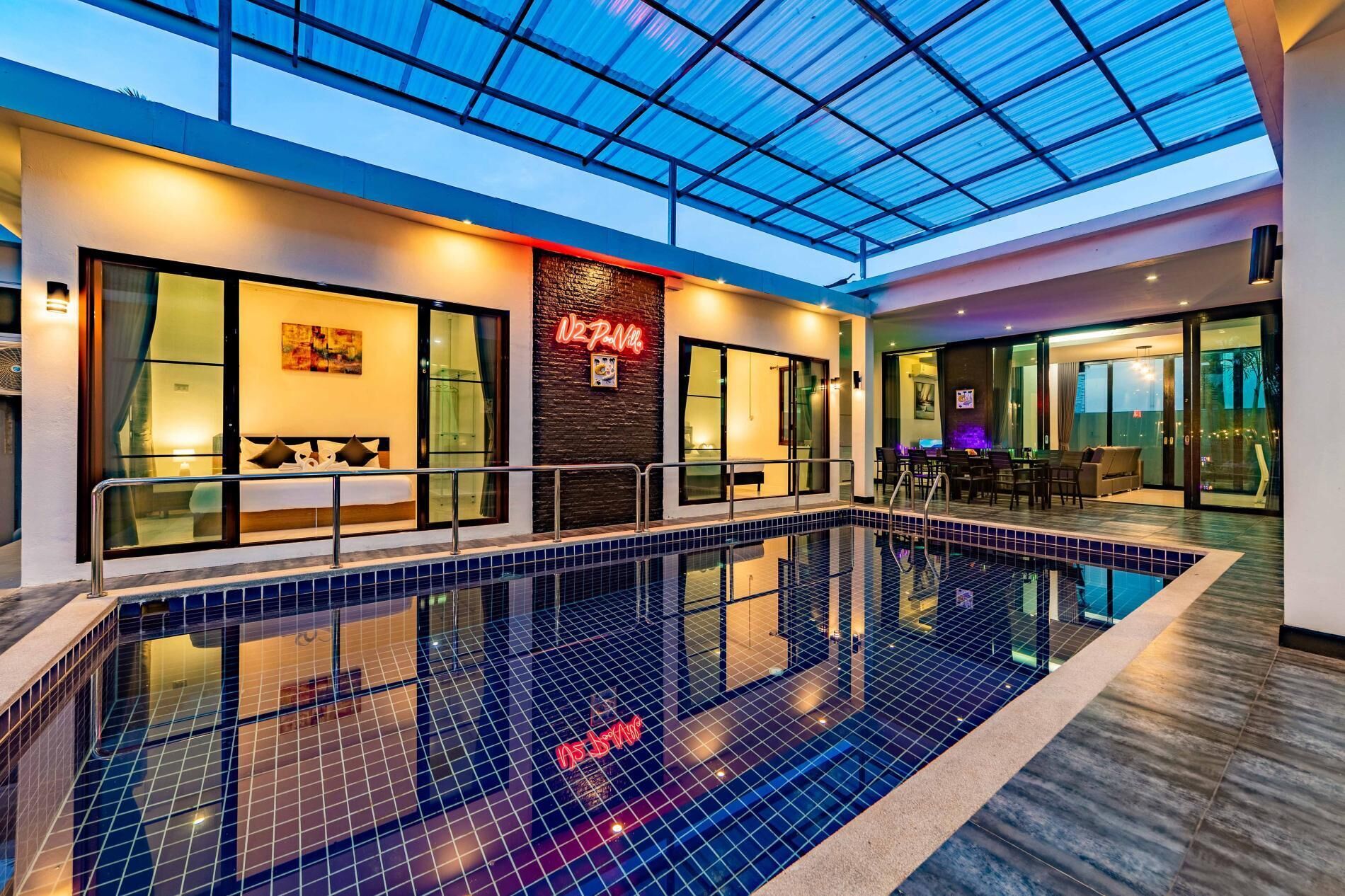 A modern indoor swimming pool with glass walls, a visible restaurant, and a seating area with a view.