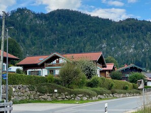 Un chalet de montagne avec un toit rouge, entouré d’une végétation luxuriante et d’un mur de pierres.