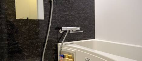 A bathroom with a bathtub, a shower, and a mirror. There are toiletries in a compartment.