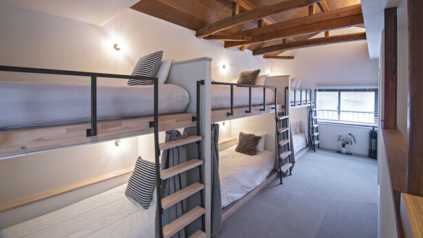 Quarto com beliche, vigas de madeira, escada e janela com persianas.