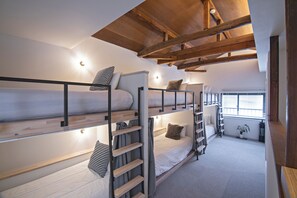 Habitació amb lliteres, bigues de fusta, escala i finestra amb persianes.