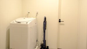 Quarto pequeno com máquina de lavar, aspirador de pó e uma porta.