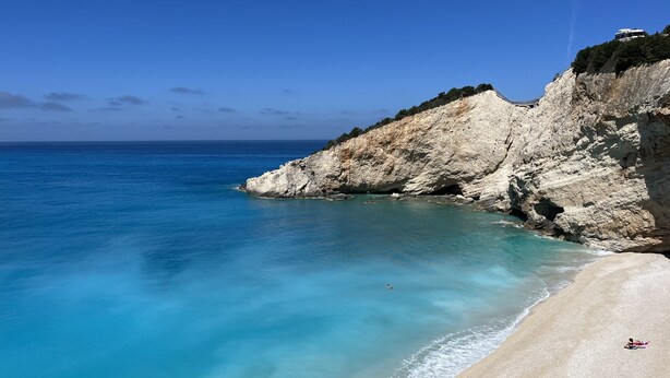 Une plage à l’eau turquoise et limpide, une falaise rocheuse et une rive sablonneuse.