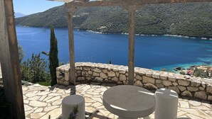 Une terrasse dallée de pierres, avec une table ronde et deux chaises, d’où l’on peut admirer un lac d’un bleu limpide et des collines verdoyantes.