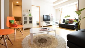 A modern living room with a white coffee table, orange and green chairs, a black sofa, and a television. - AMS TOWER (Sapporo)