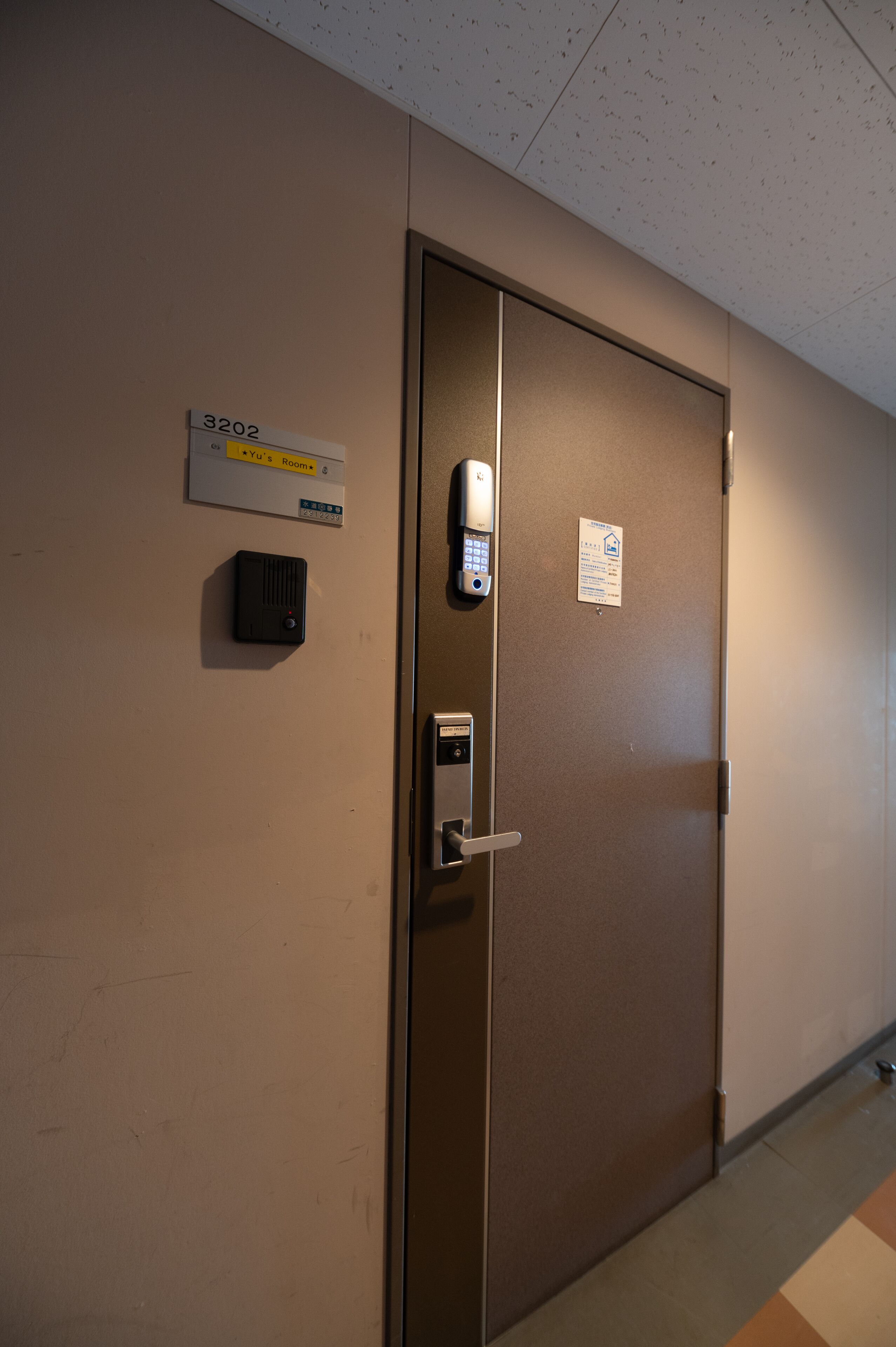 Porta de quarto de hotel com fechadura por teclado, placa indicando o número do quarto 3202 e um pequeno dispositivo fixado na parede.