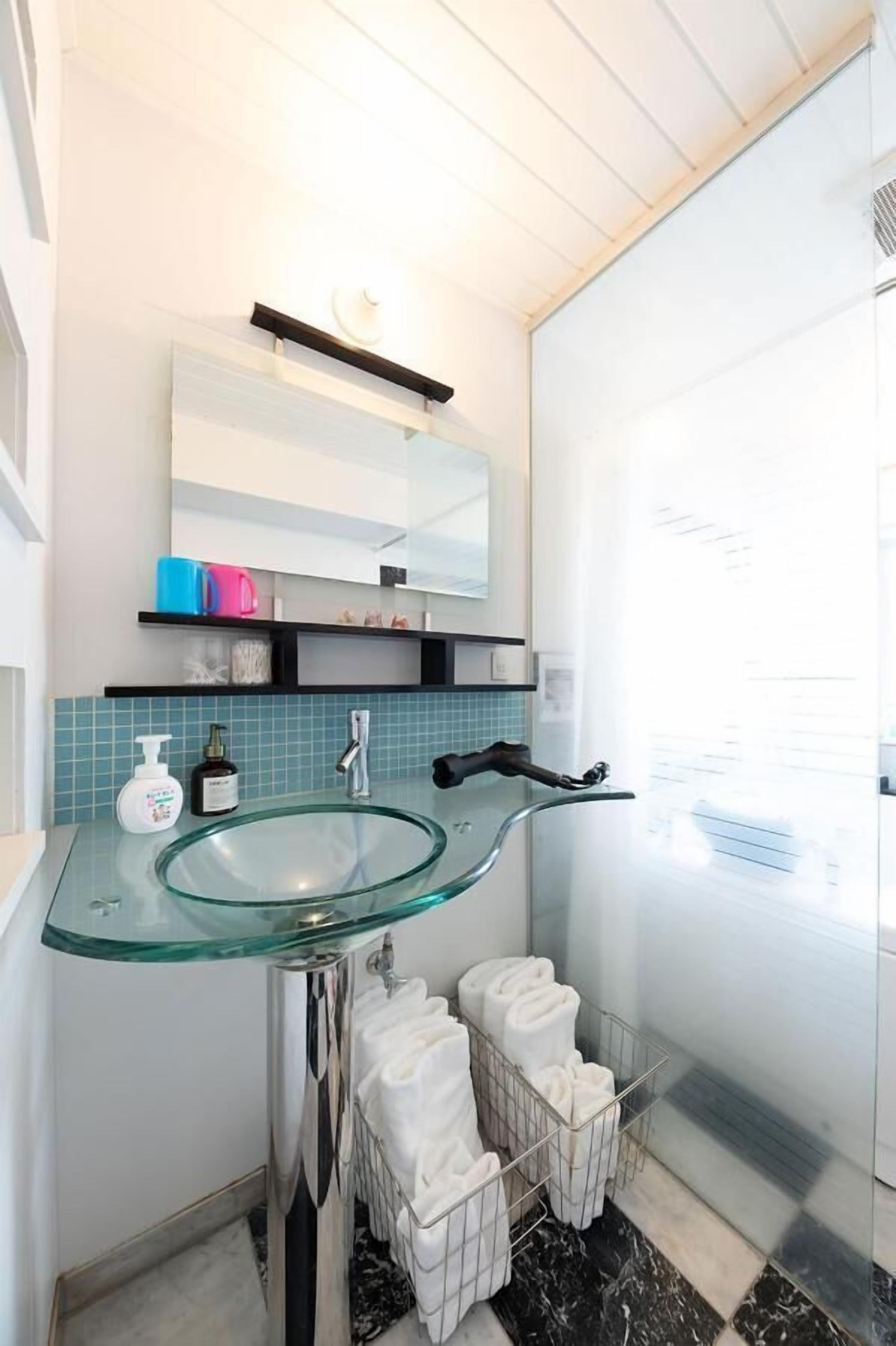 A modern bathroom with a glass sink, a mirror, and a towel rack.