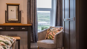 A bedroom with a bed, a dresser, a chair, a window with curtains, and a view of the countryside. - The Lee - Luxury Cottages (Keighley)