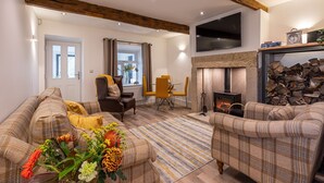 A living room with a fireplace, a sofa set, a dining table with chairs, and a television mounted on the wall. - The Lee - Luxury Cottages (Keighley)