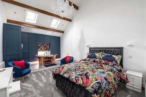 A bedroom with a large bed, a blue chair, a desk, and a chandelier.