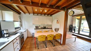 A kitchen with white cabinets, a dining table with yellow chairs, a clock, and a window with a view of the outdoors.