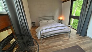 A bedroom with a metal bed frame, white bedding, a small bedside table, and a window with curtains.