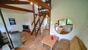 A compact living space with a loft area, a kitchen visible through a window, and a round mirror on the wall.