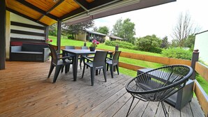 An outdoor deck with a wooden floor, a table with chairs, and a wicker chair.