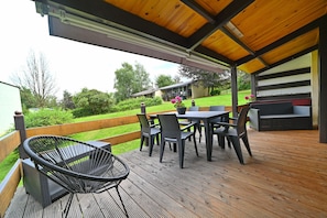 Un patio al aire libre techado con piso de madera, una mesa con sillas y una silla de mimbre.