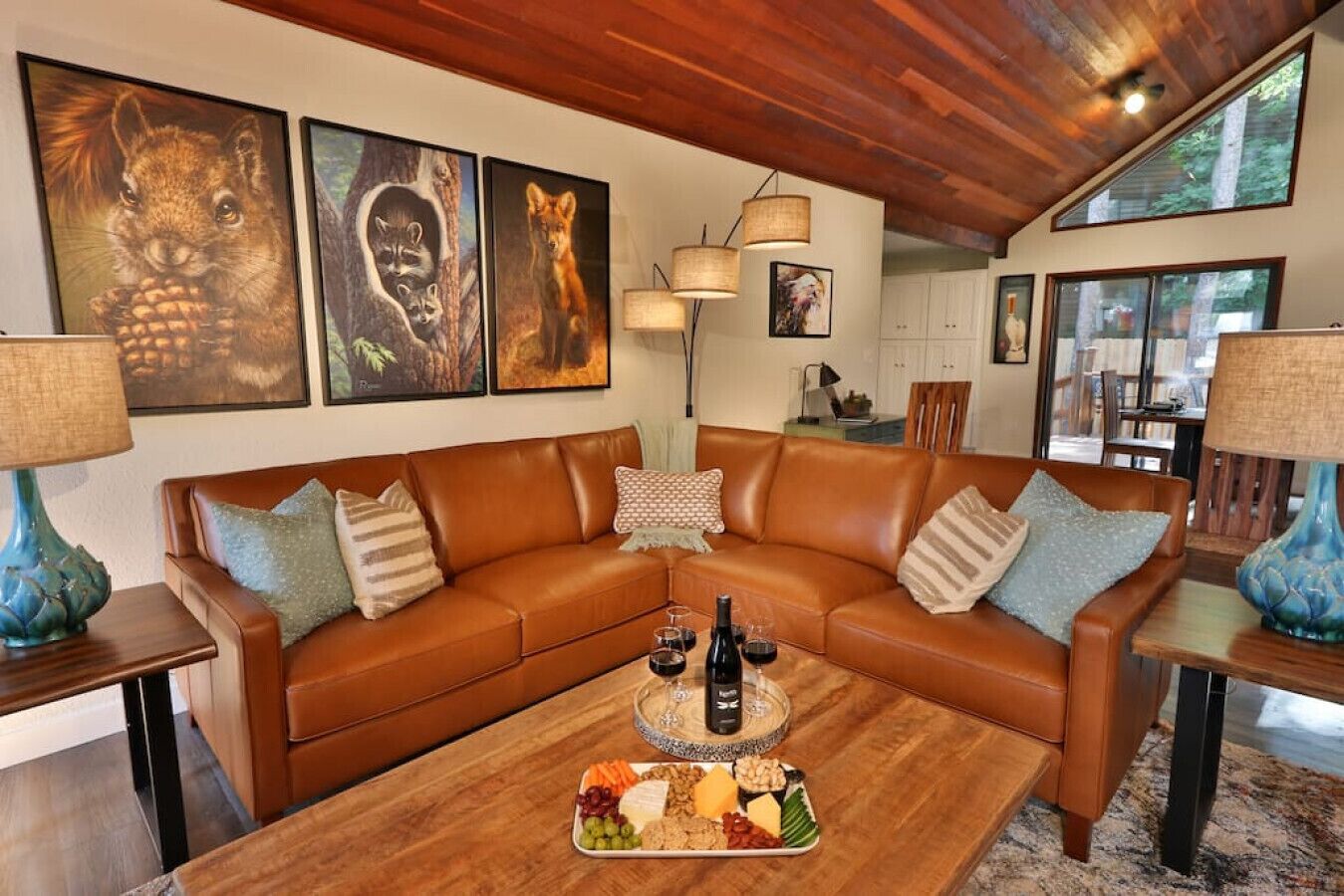 A cozy living room with a brown leather sectional sofa, a wooden coffee table with a fruit platter, and framed wildlife art on the wall.