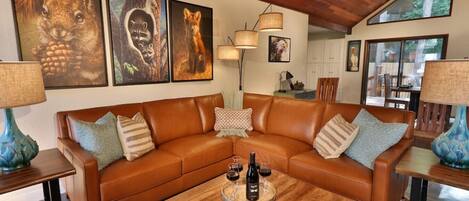 A cozy living room with a brown leather sectional sofa, a wooden coffee table with a fruit platter, and framed wildlife art on the wall.
