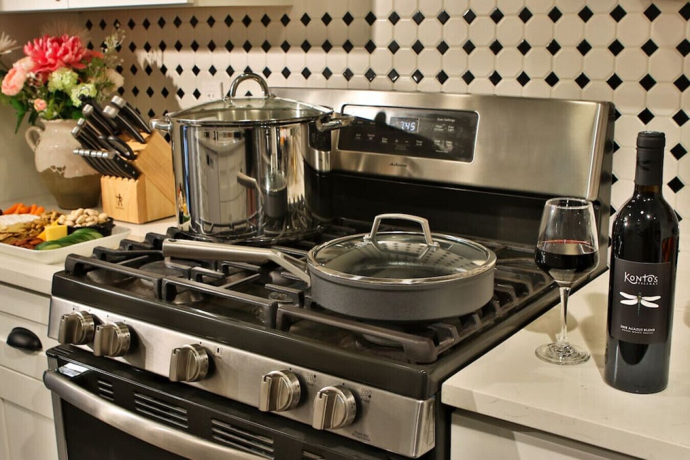 A kitchen with a stainless steel stove, pots, a wine bottle, and a glass of wine.