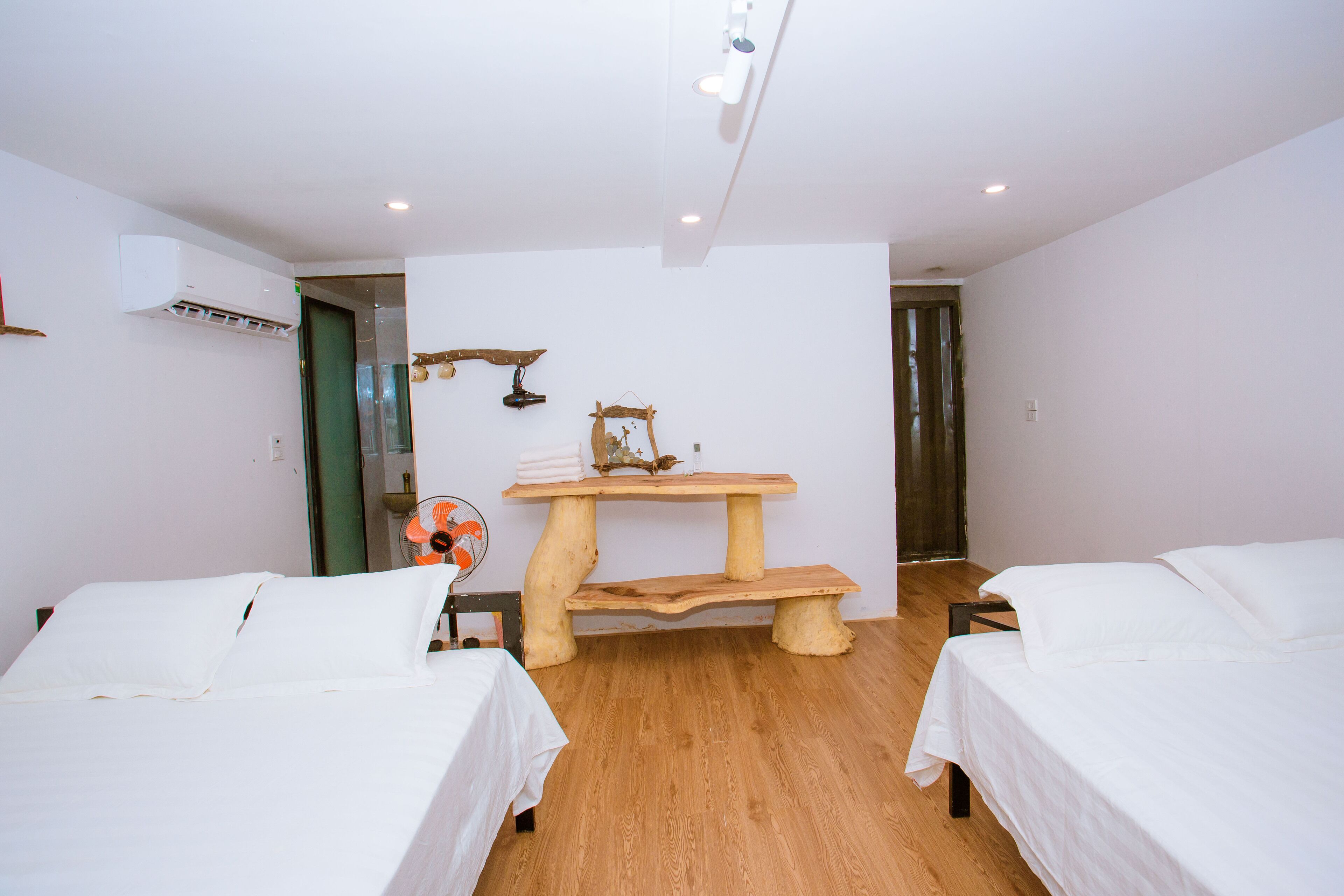 A room with two beds, a wooden bench, a fan, and a wall-mounted air conditioner.