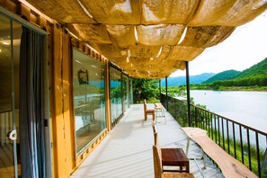 A balcony with a view of a lake and mountains, wooden furniture, and a covered area with a roof. - A Little Leaf Homestay  (Phong Nha)