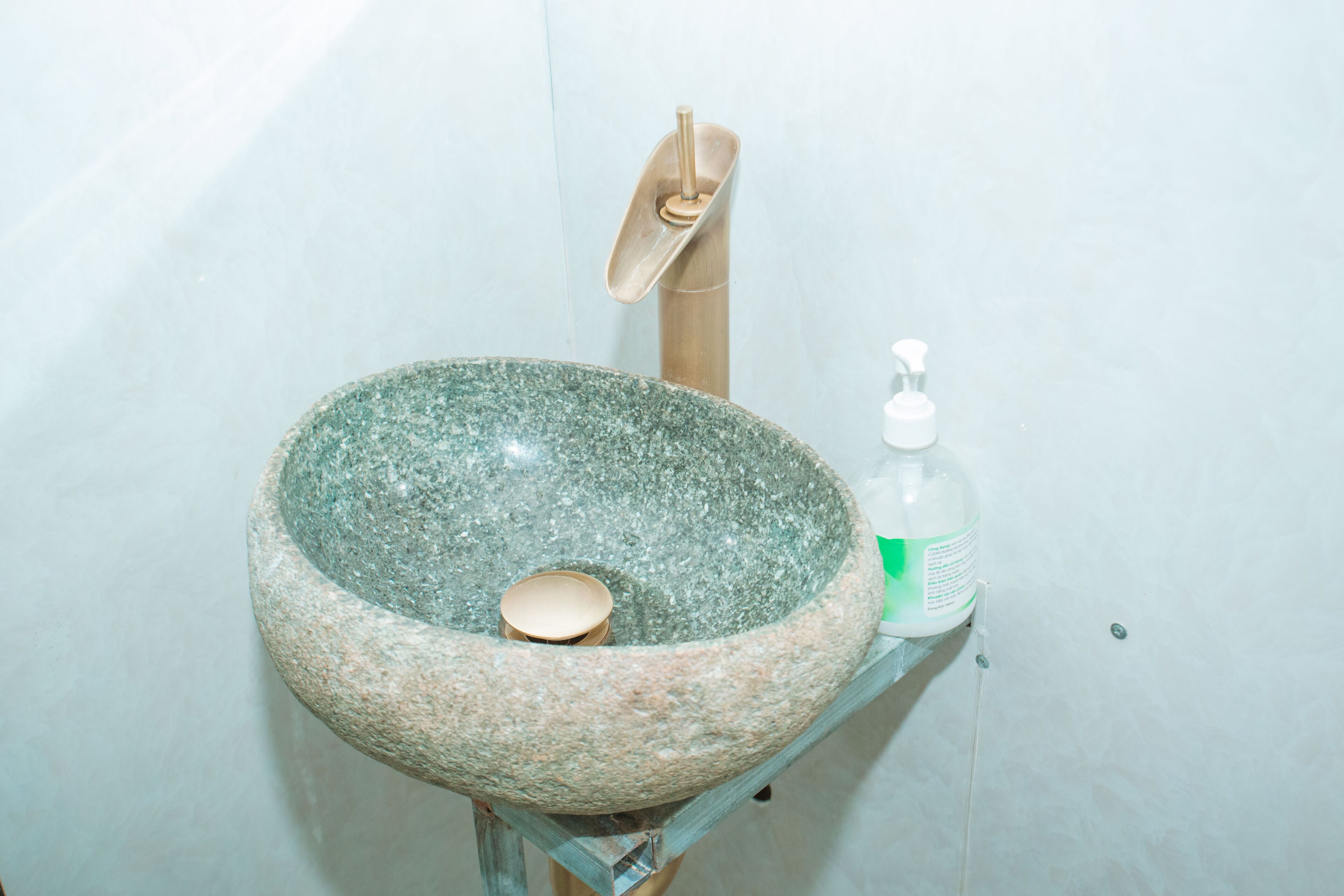 Un lavabo de piedra con un pomo de madera y un dispensador de jabón sobre una repisa de vidrio.