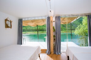 A bedroom with two beds, a balcony with a view of a lake and greenery, and a wooden ceiling structure. - A Little Leaf Homestay  (Phong Nha)