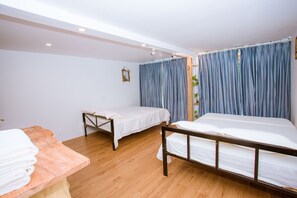 A room with two beds, wooden flooring, a wooden table with towels, and a window with blue curtains. - A Little Leaf Homestay  (Phong Nha)