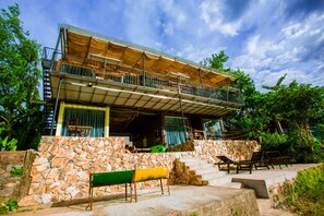 A two-story building with a balcony, stone walls, and outdoor seating. - A Little Leaf Homestay  (Phong Nha)