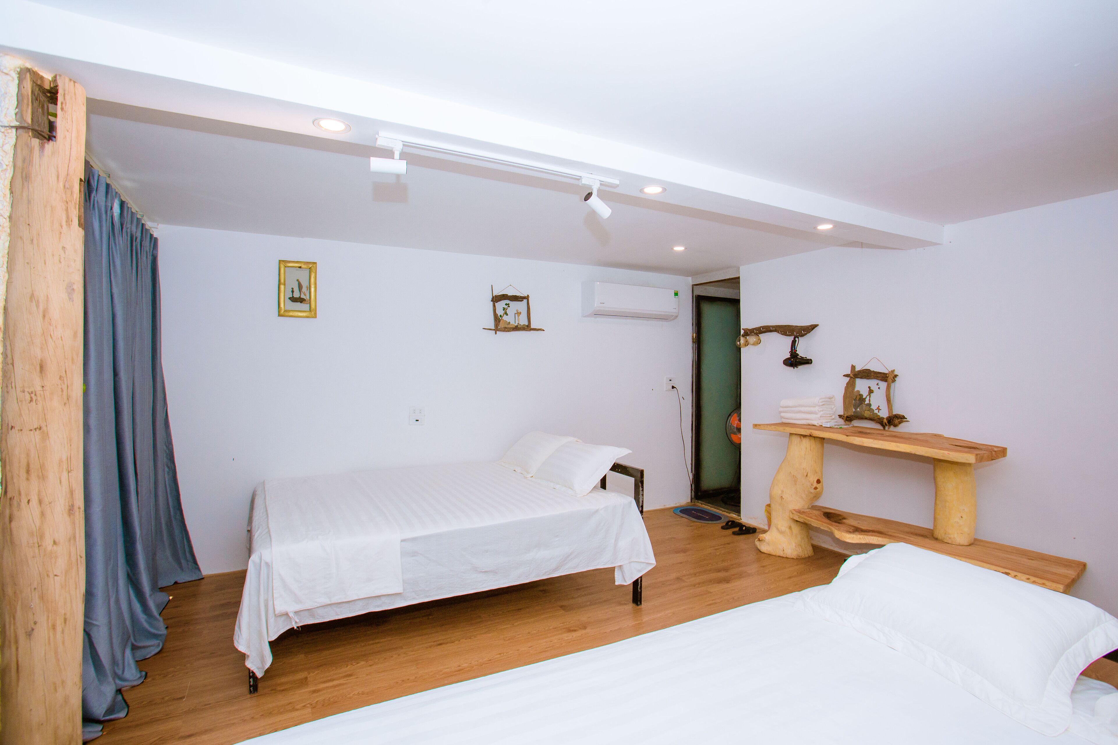 A bedroom with two beds, wooden flooring, a wooden bench, and a wall-mounted air conditioner.