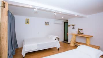 A bedroom with two beds, wooden flooring, a wooden bench, and a wall-mounted air conditioner.