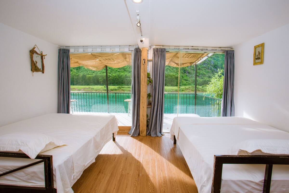 Una habitación con dos camas, piso de madera, un ventanal con cortinas y vista a una piscina.