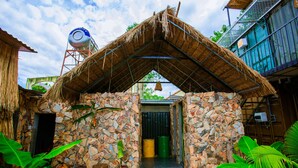 A stone-walled building with a thatched roof, a water tank, and potted plants. - A Little Leaf Homestay  (Phong Nha)