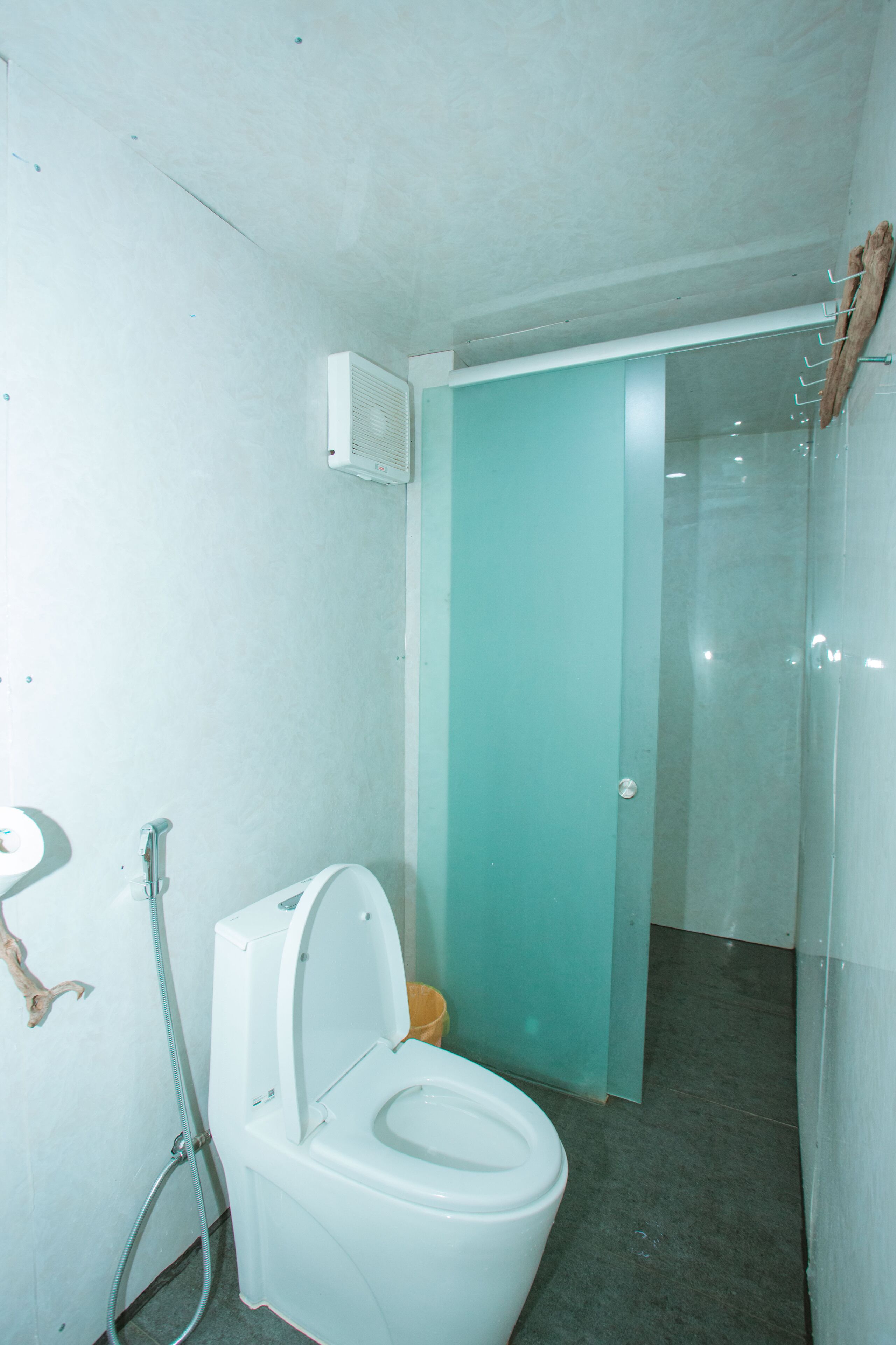 Een badkamer met een toilet, een douche en een glazen deur die naar een andere kamer leidt.