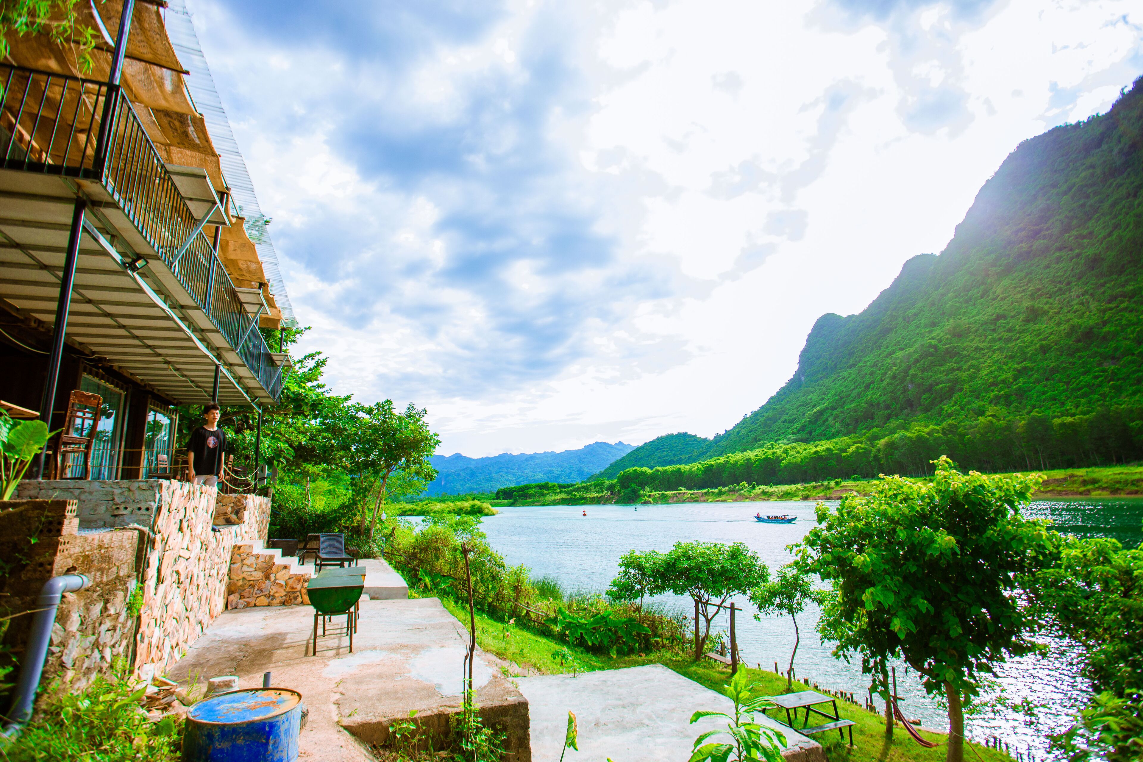 A riverside view with a stone staircase leading to a balcony, a green chair, and a table.