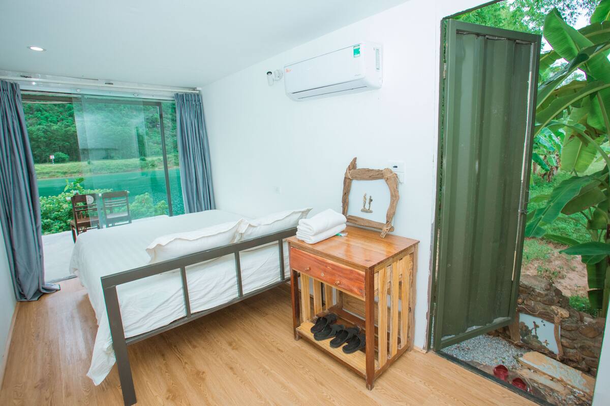 Un dormitorio con una cama, una mesita de noche de madera, un espejo y una ventana con cortinas.