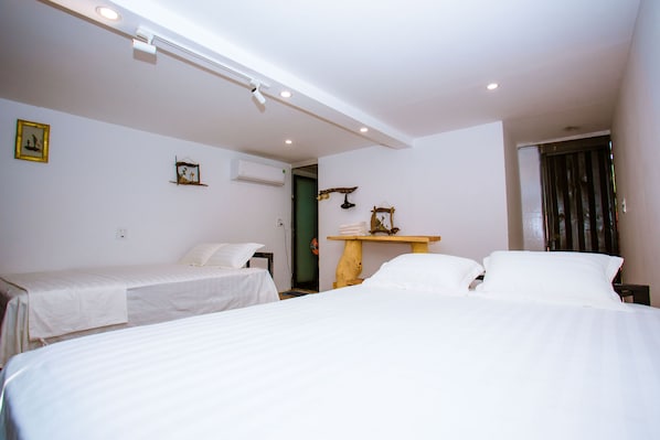 A hotel room with two single beds, a wooden nightstand, and a small table with a lamp. - A Little Leaf Homestay  (Phong Nha)