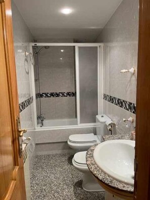 Une salle de bain avec douche, toilettes et lavabo.