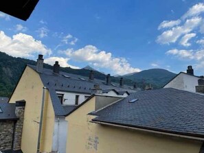 Un bâtiment doté d’un toit en pente, de plusieurs cheminées et ayant une chaîne de montagnes en arrière-plan.