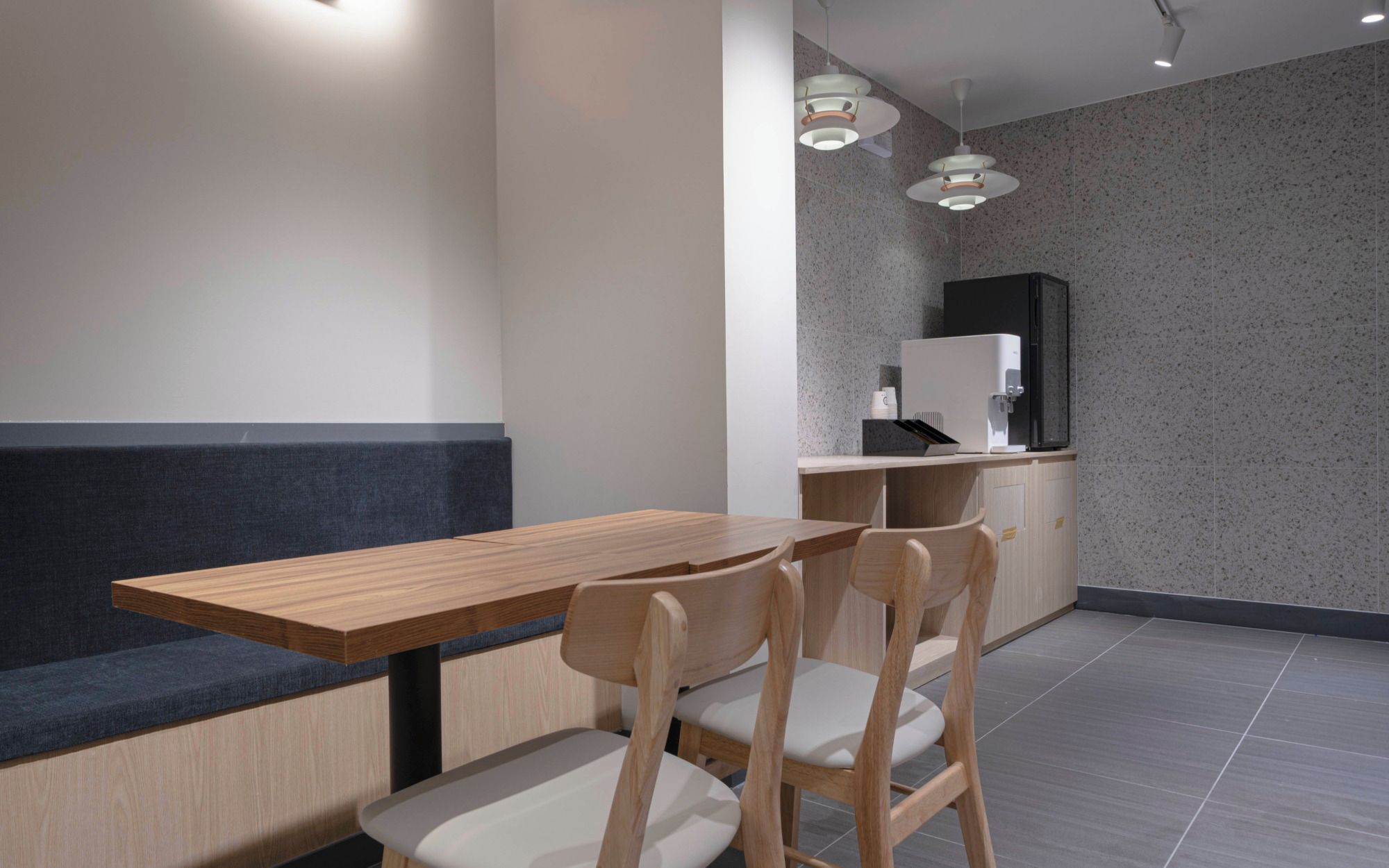 Un interior moderno con una mesa de madera y dos sillas, un banco oscuro y una zona de kitchenette.