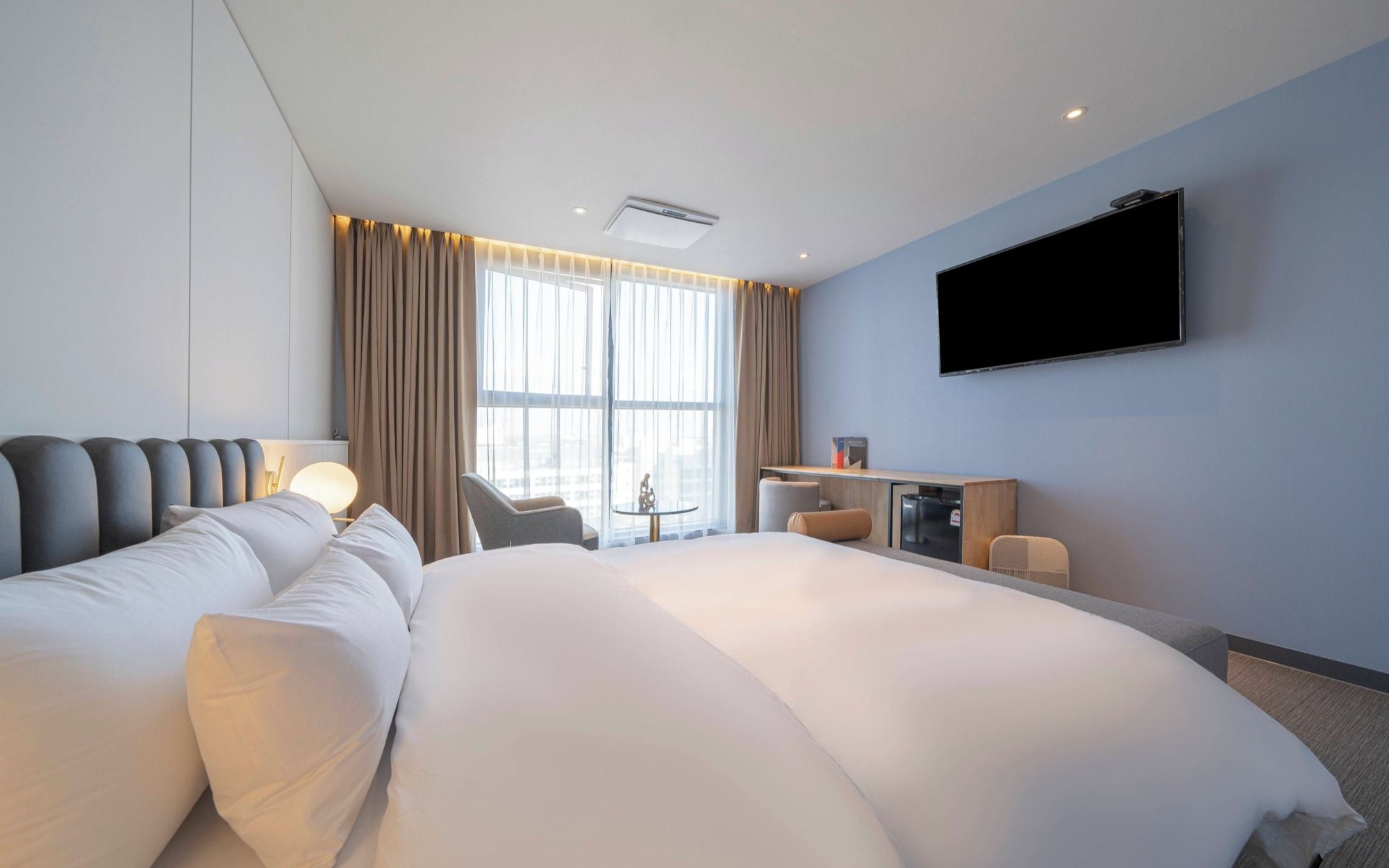 Habitación de hotel moderna con una cama grande, un escritorio, un televisor de pantalla plana y vistas de la ciudad a través de amplias ventanas.