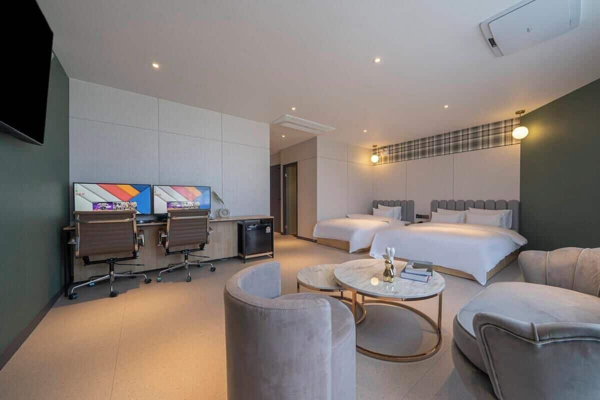 A modern hotel room with a desk, two beds, a sofa, and a TV.