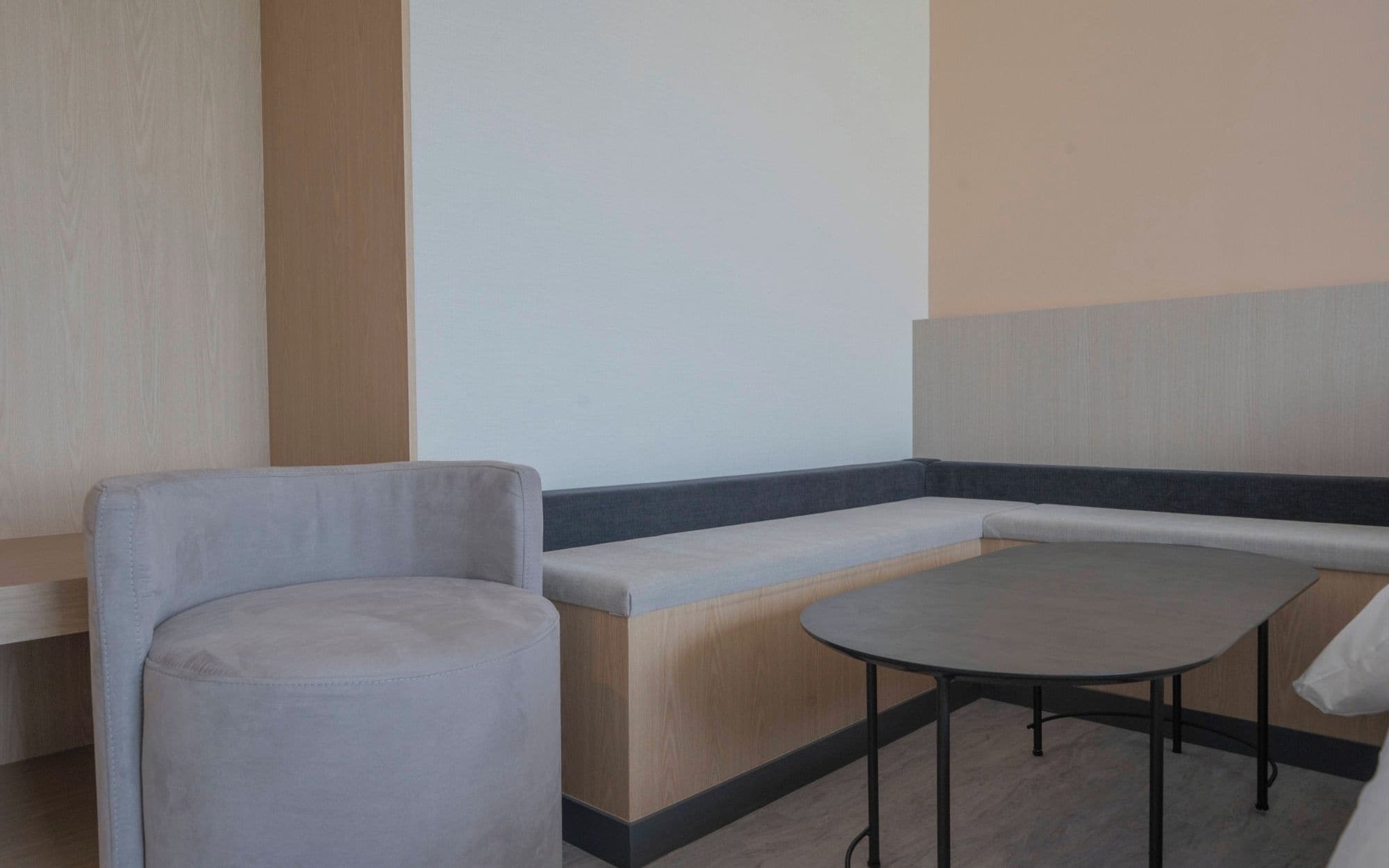 Una zona de estar con un banco y una mesa redonda, suelo de madera y una pared con panel vertical de madera.