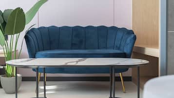 Ein blaues, gepolstertes Sofa mit einem Marmortisch davor, einer Topfpflanze und einem Holzkabinett in einem modernen Interieur.