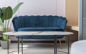 Un sofá tapizado azul con una mesita de mármol al frente, una planta en maceta y un armario de madera en un interior moderno.