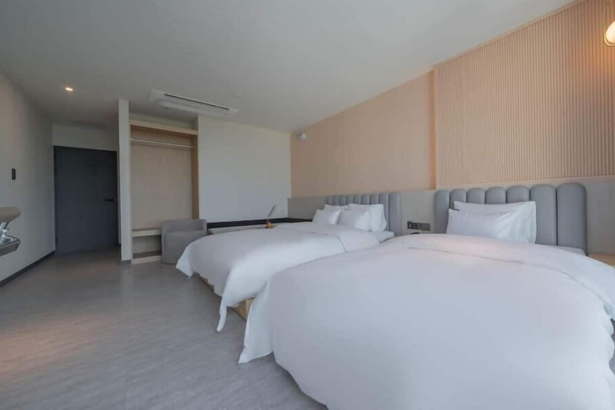 A hotel room with two beds, a walk-in closet, a bedside table, and a wall-mounted light fixture.
